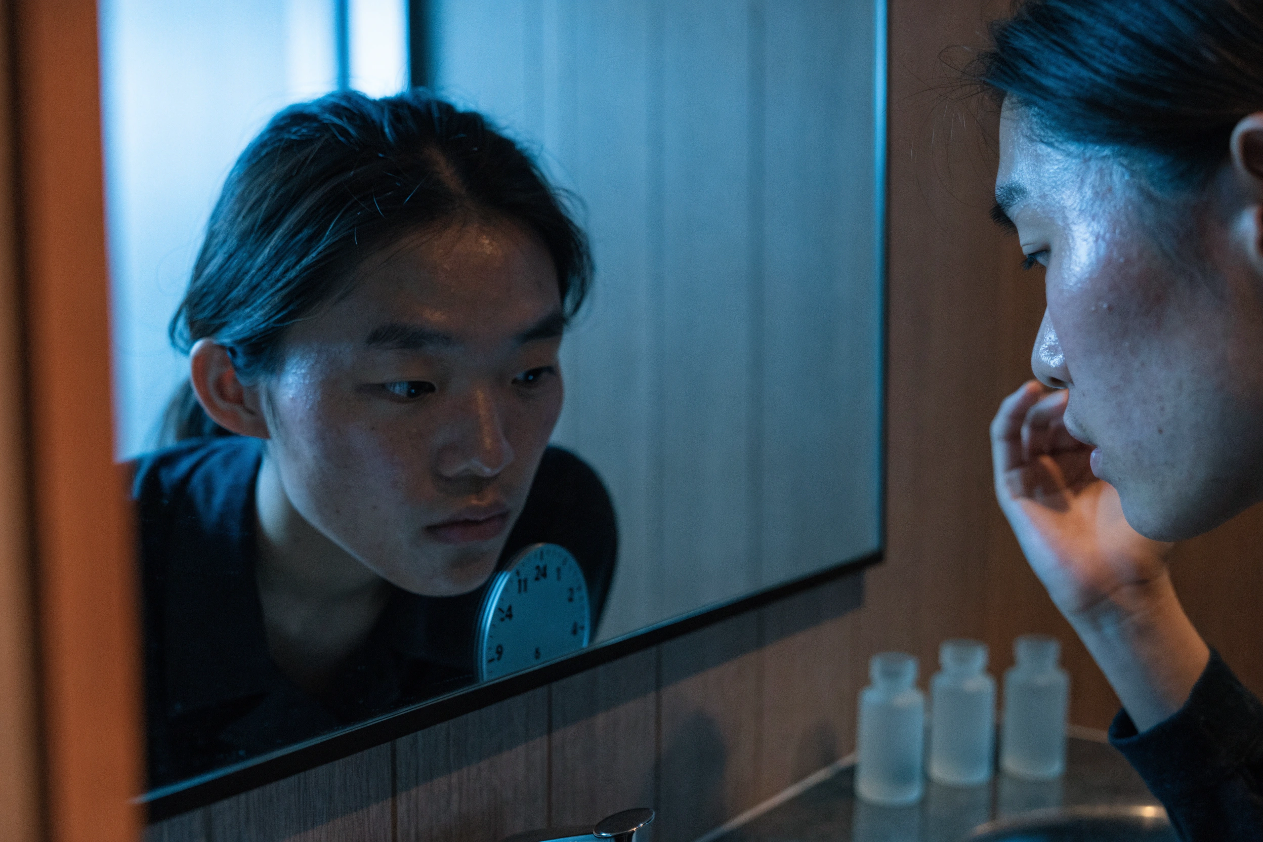 A traveller faces a hotel mirror while the local-time card sits beside the basin.
