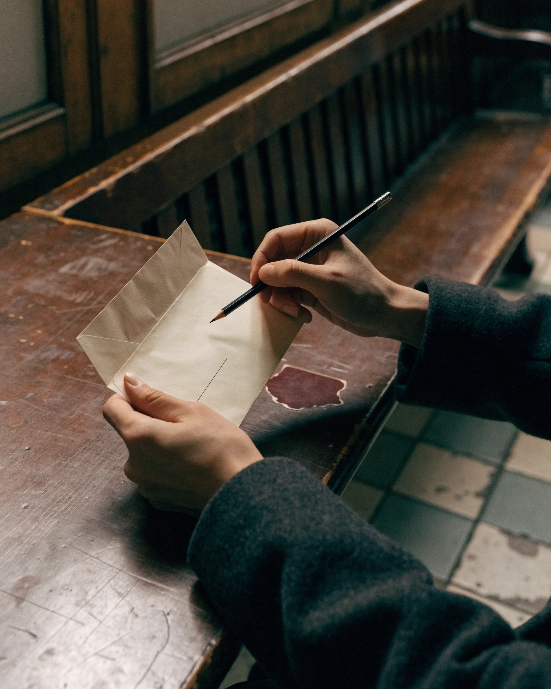 A pen hovers above the address line while the writer's other hand closes the page.