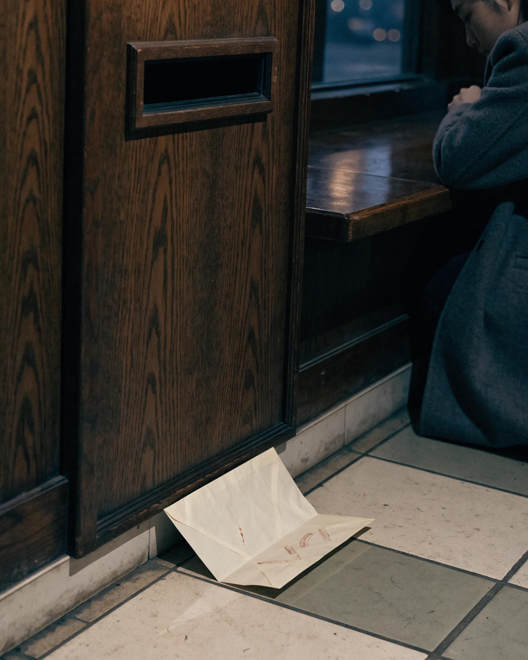 An empty mail slot faces a returned envelope on the tiled floor below.