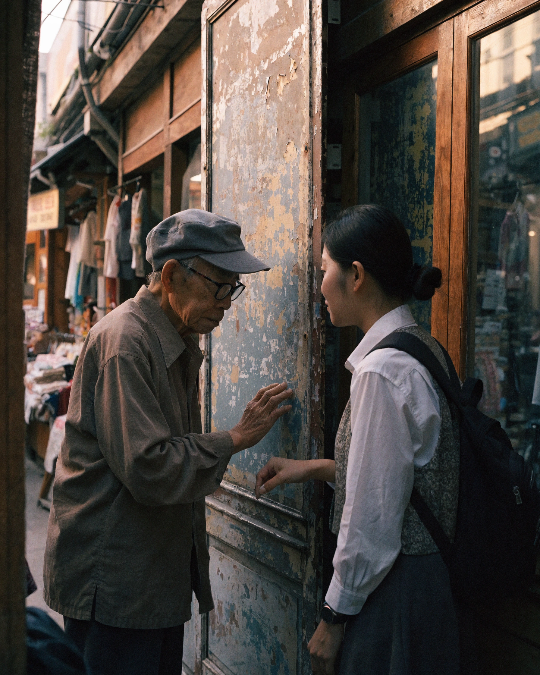 An older shopkeeper describes a sign while a younger recorder listens beside it.