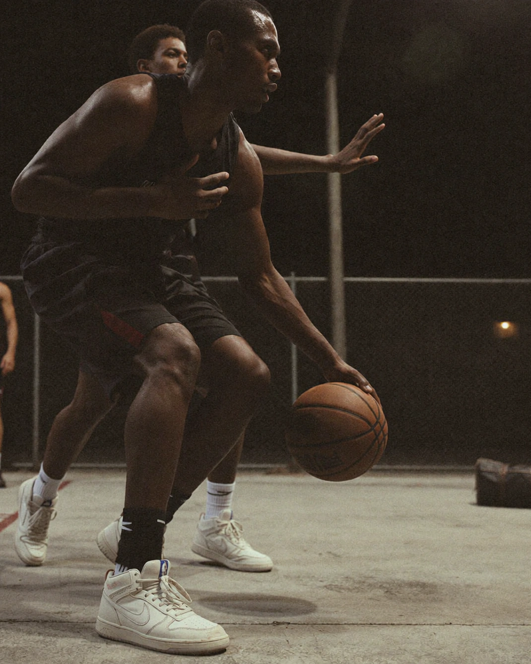 A basketball player dribbles on an indoor court with two other players close behind.