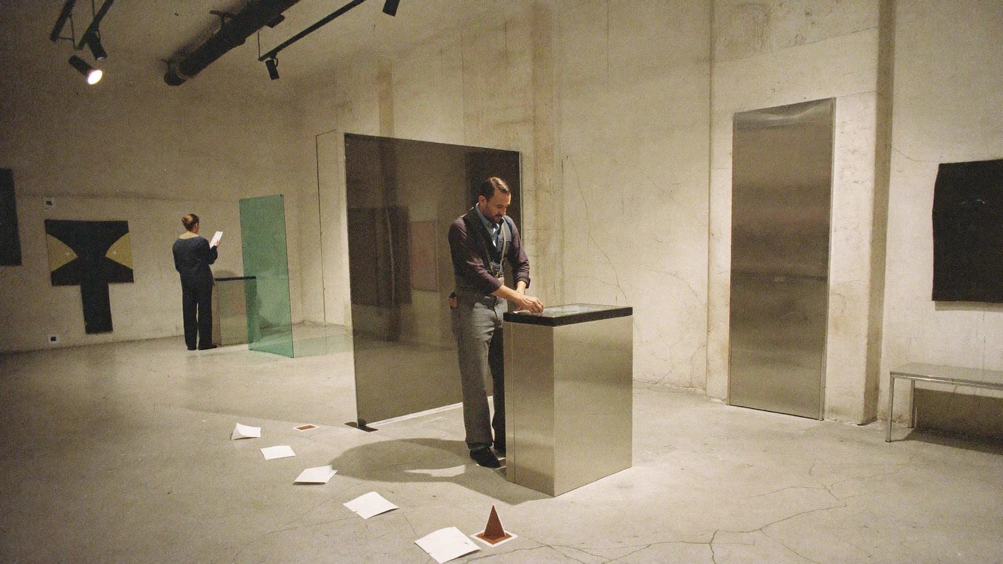 A person arranges a low display plinth and green metal panel inside a spare gallery room.