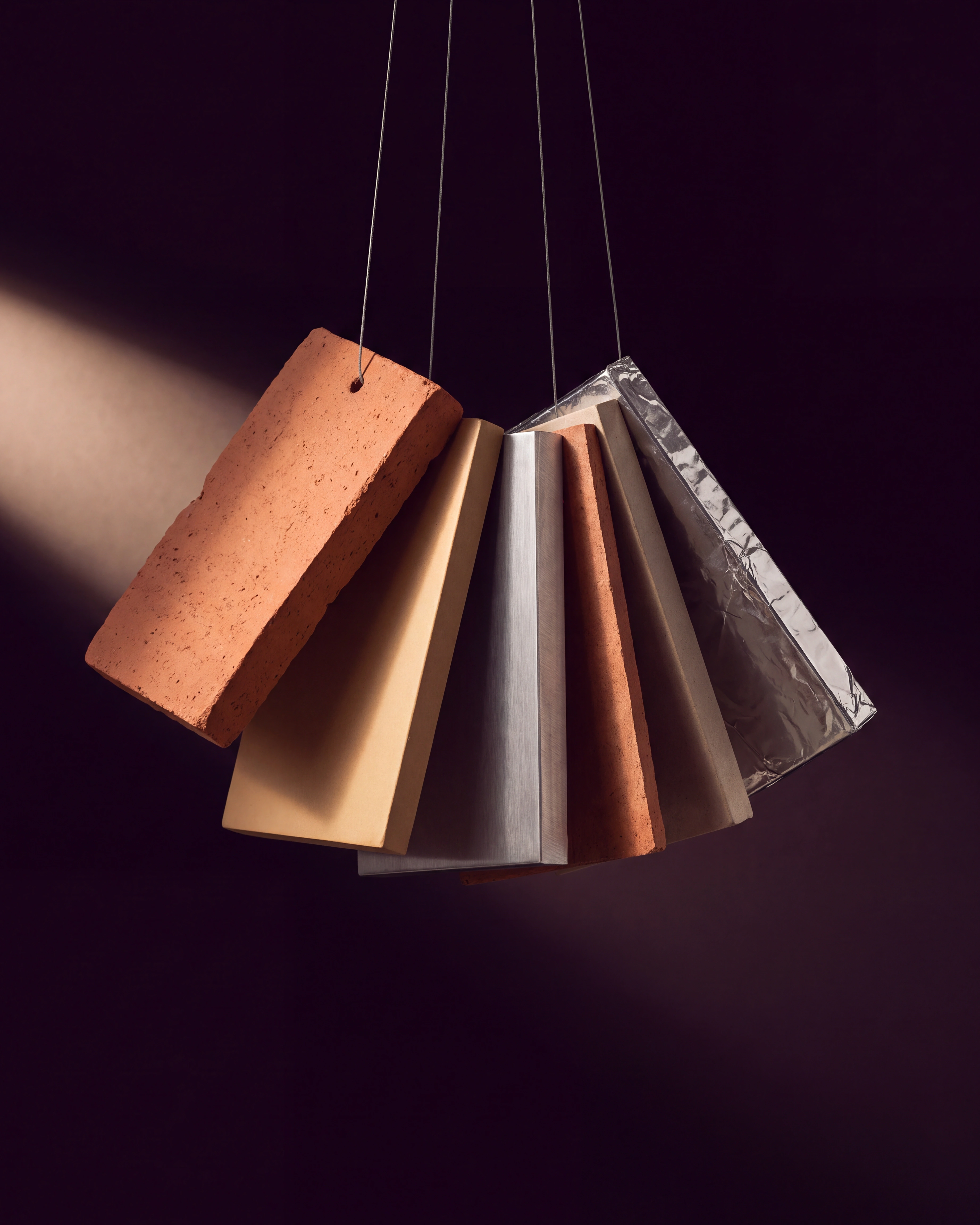 Rectangular clay, metal, brown, and foil material samples suspended in a fan against a dark plum background.